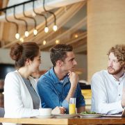 Three young professionals engaged in a discussion at a modern office cafeteria.