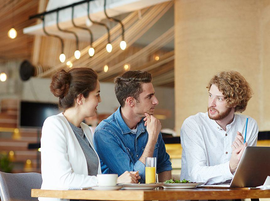 Three young professionals engaged in a discussion at a modern office cafeteria.
