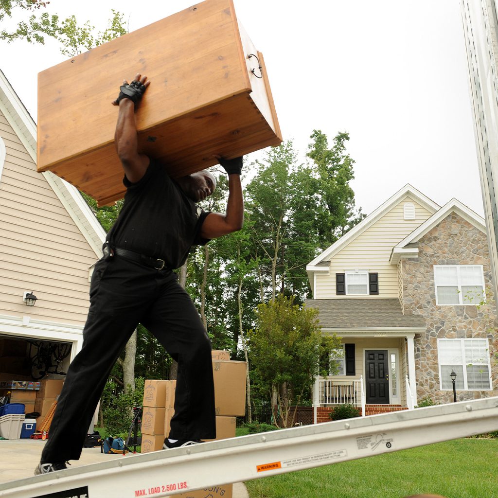 Mover carrying a wooden box up a ramp into a house.