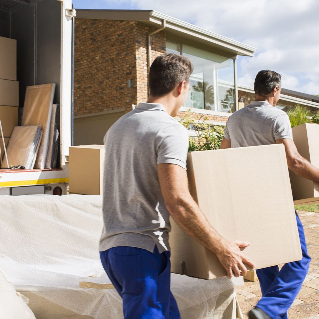 Two movers carrying a large box outside a house.