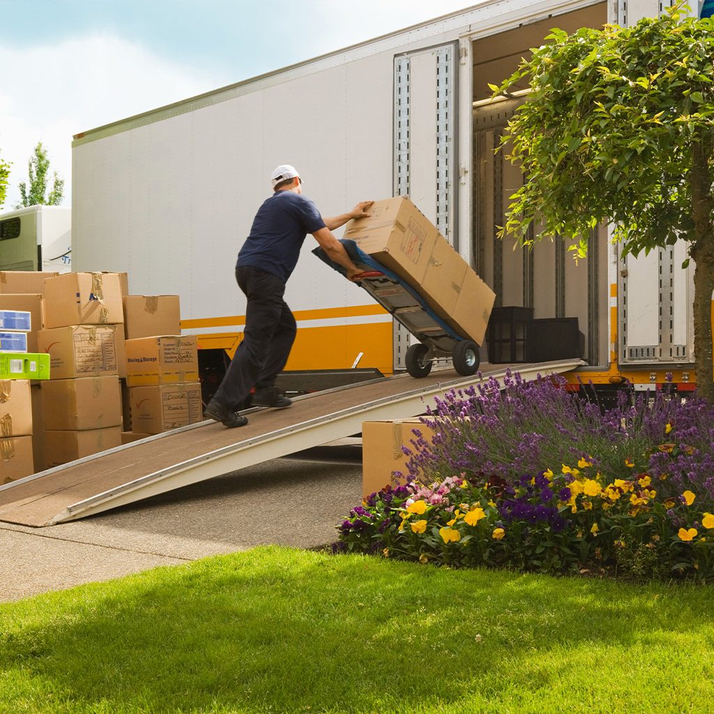 Man unloading boxes from a truck using a hand truck on a ramp.