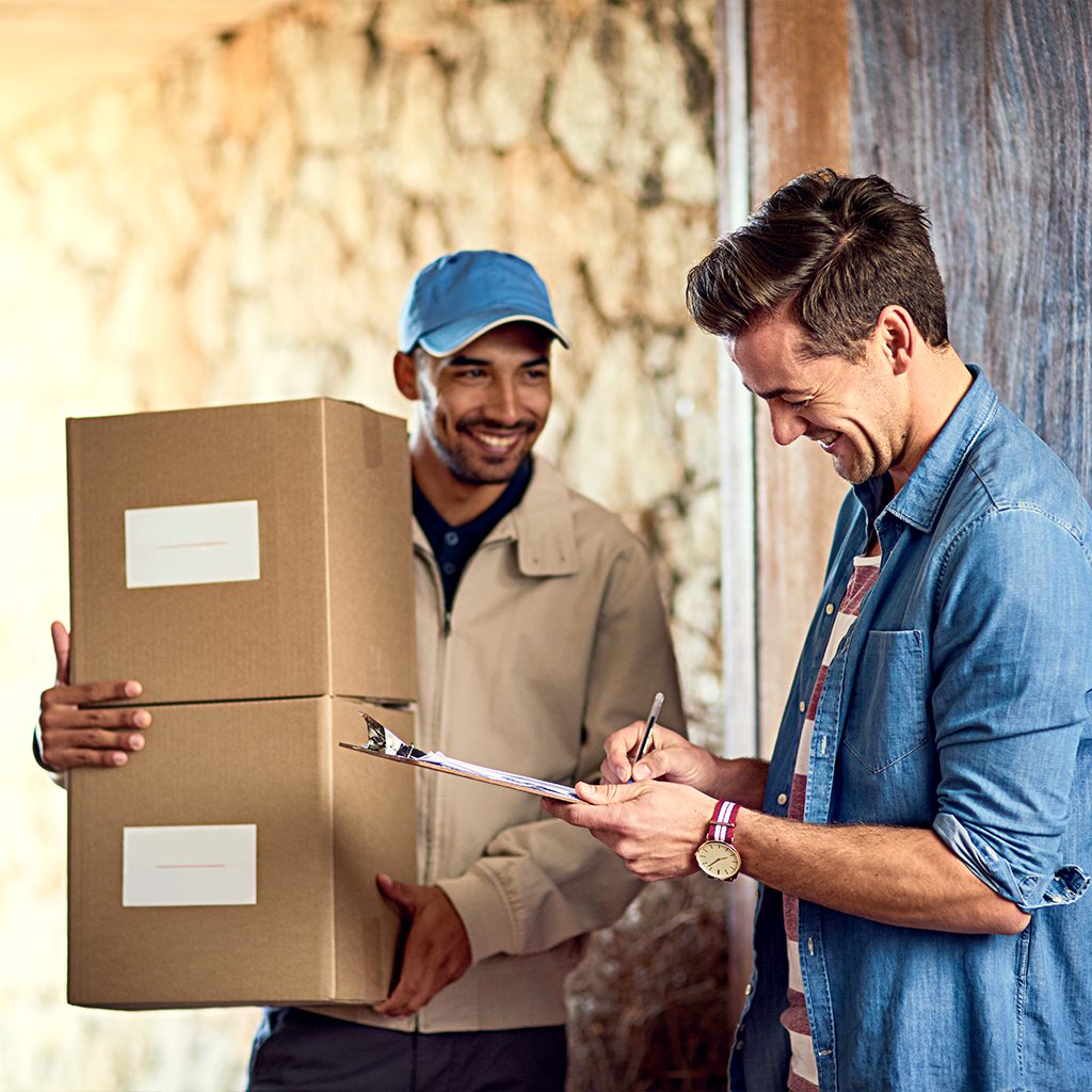 Two men smiling while handling moving boxes together.