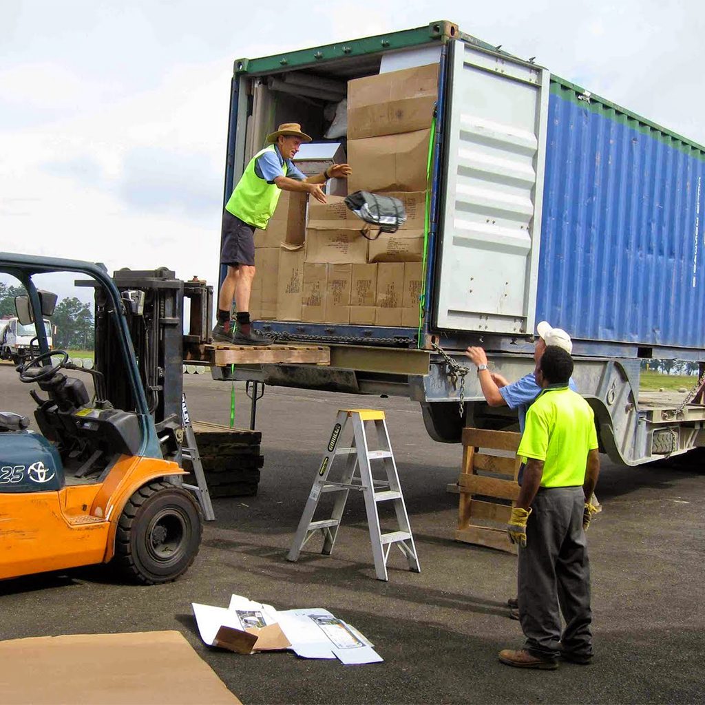 Workers loading boxes into a shipping container using a forklift and ladder.
