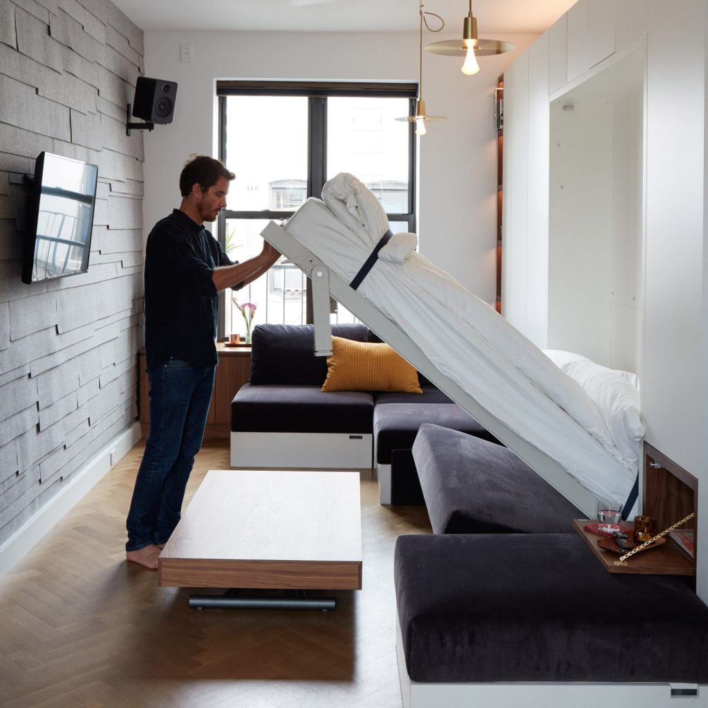 Man unfolding a hidden bed from a wall in a modern living room.