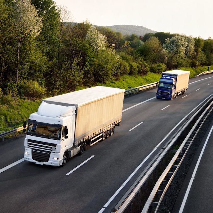 Two large trucks driving on a highway surrounded by greenery.