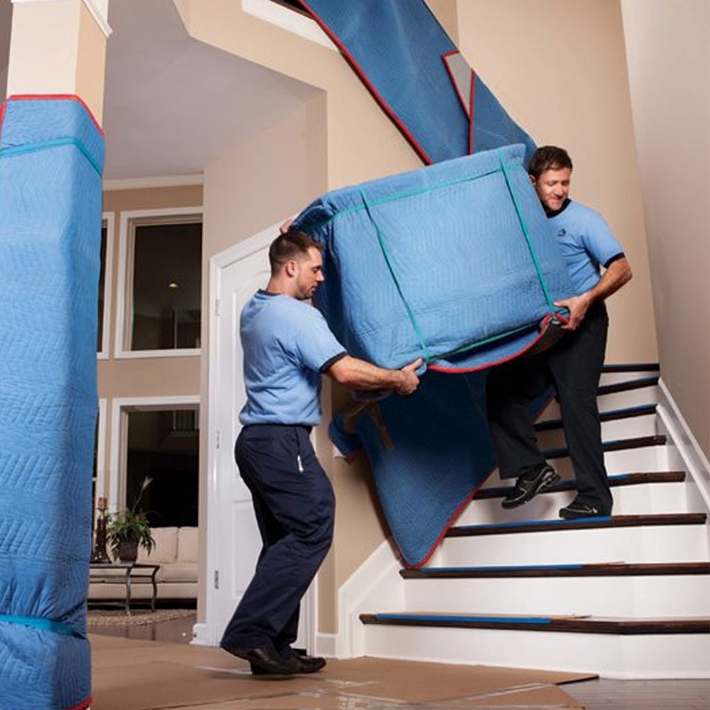 Two movers carry a couch up a staircase.