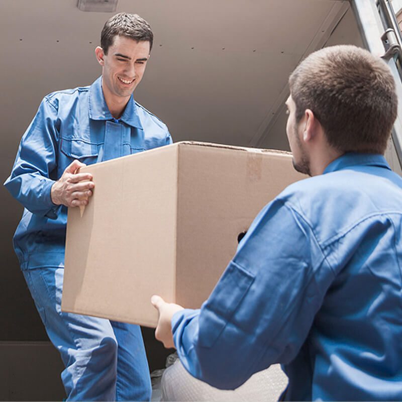 Two men in blue uniforms lifting a large cardboard box together.
