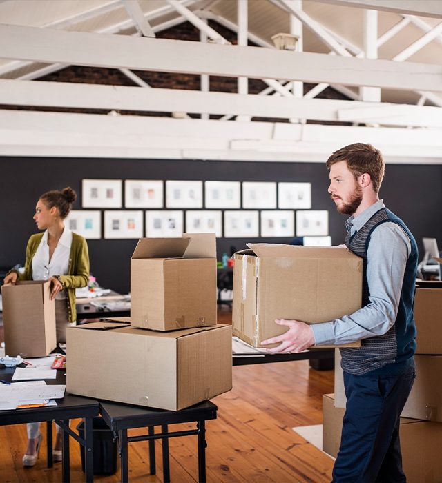 Two people packing cardboard boxes in a bright office space.