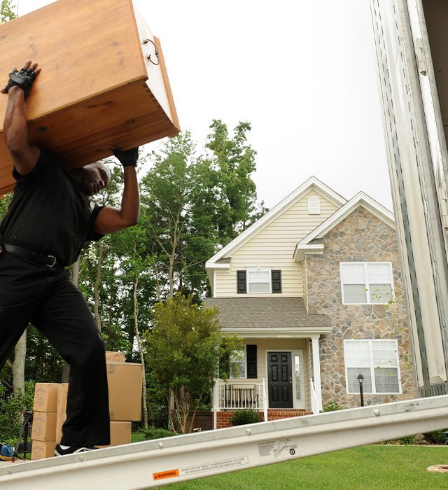 Mover carrying a large wooden box up a ramp to a house.